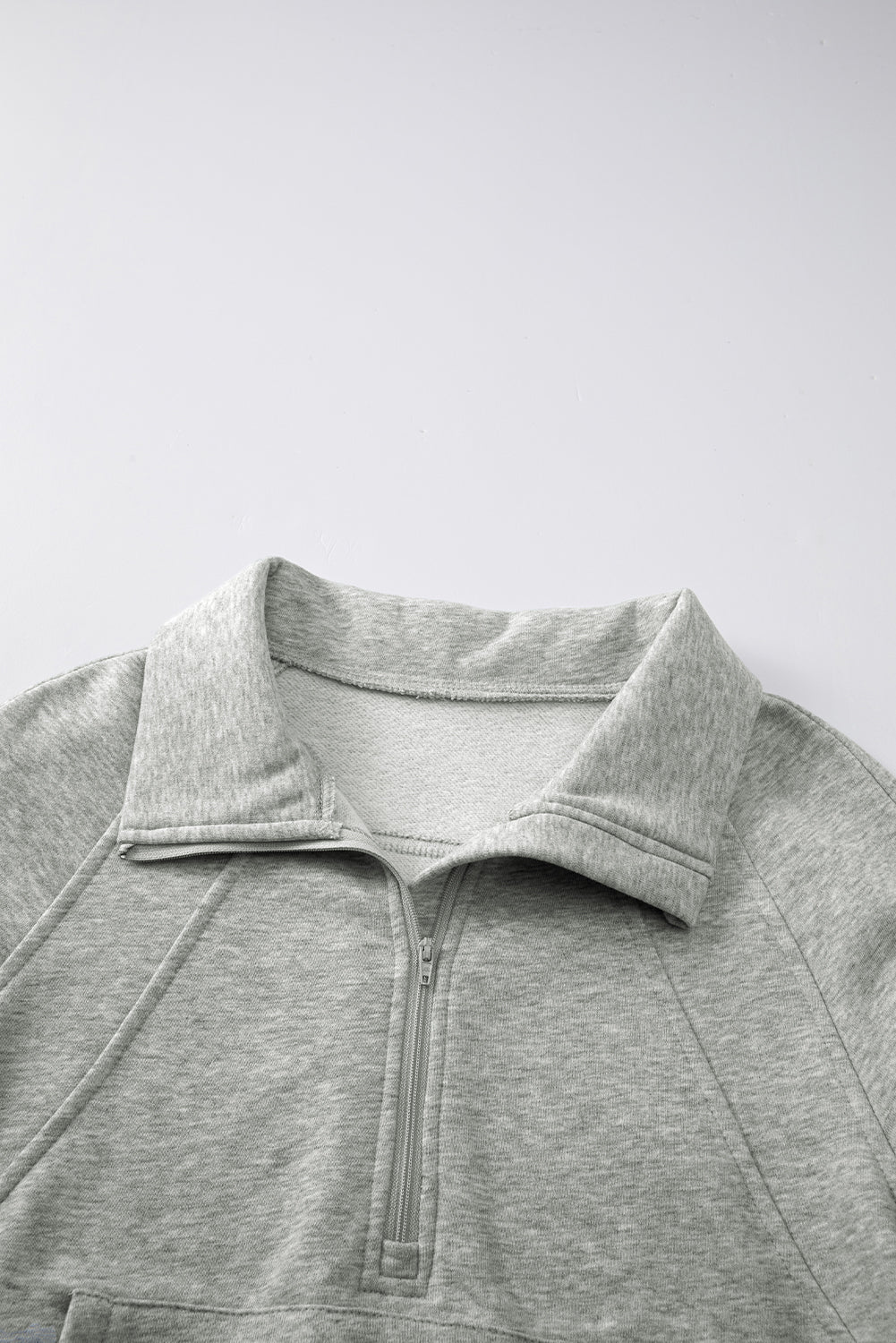 A person wears a gray, zip-up stand collar sweatshirt with ribbed thumbhole sleeves from Shewin, paired with white shorts.