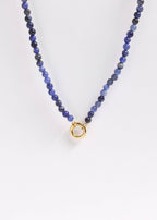 The WJW Semi Precious Natural Stone Charm Keeper Necklace showcases round blue semi-precious stones and is finished with an elegant circular clasp coated in 18K Gold PVD, beautifully presented against a plain white background.