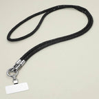 A Rhinestone Phone Lanyard Necklace by Sensibling Corp. with a sleek black strap, silver clasp, and an attached blank rectangular name tag is displayed on a plain light surface.