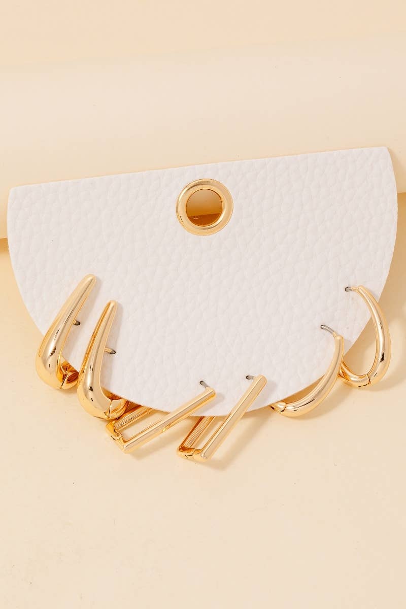 The Anarchy Street Mixed Long Oval Hinge Hoop Earrings Set showcases five pairs of gold hoops with an elegant oval hinge design on a white textured semicircular card with a central hole, displayed against a beige background.