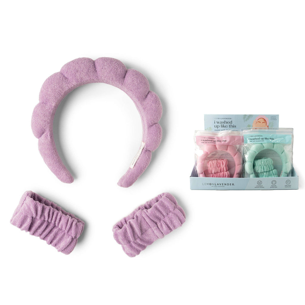 A lavender I Washed Up Like This Super Soft Dryband Set with matching wristbands for washing face, shown alongside a display box containing additional sets in pink and mint green.