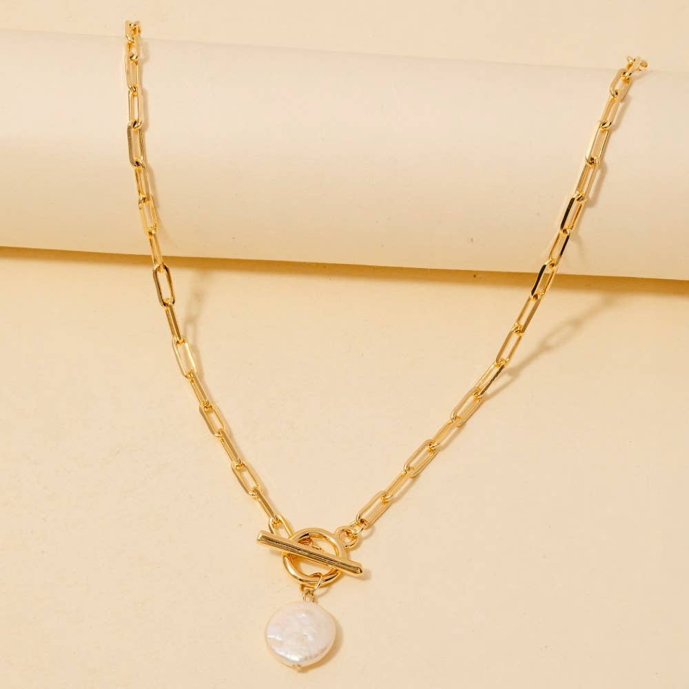 The Anarchy Street Toggle Chain Link Disc Pearl Charm Necklace features rectangular links and a round white pearl charm, displayed on a light beige surface—a chic update to the classic pearl necklace.