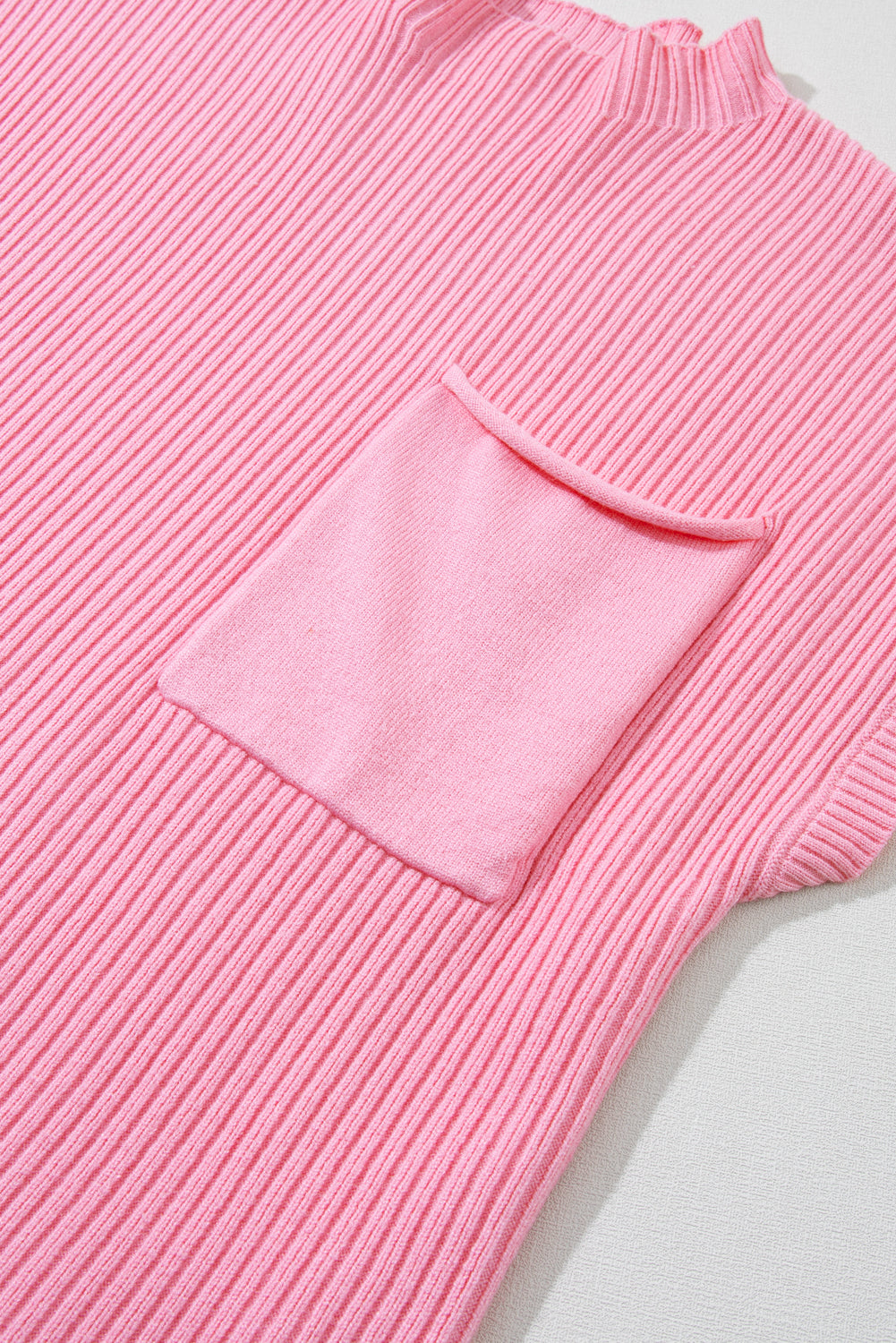 The Shewin Patch Pocket Ribbed Knit Short Sleeve Sweater in pink, ideal for transitional weather, features a large front pocket and is laid flat.