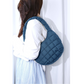 A person with long hair, wearing a white blouse and a blue plaid skirt, carries the Zenana Puffer Quilted Mini Bag in assorted colors with a comfortable shoulder strap over their shoulder.