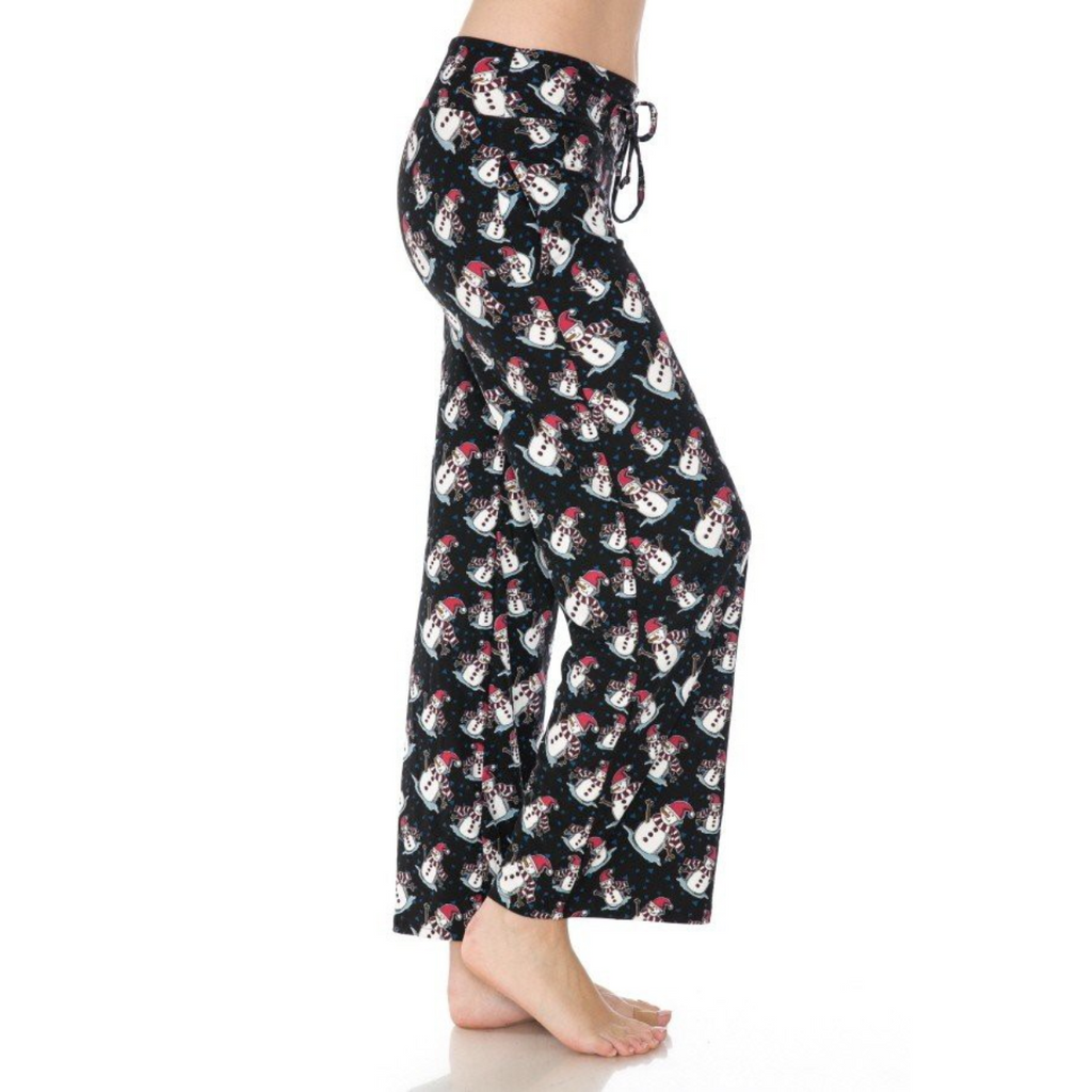 Standing barefoot on a white background, a person wears FASHION GO's buttery soft, black pajama pants adorned with a snowman pattern. These cozy pajama pants, officially named "Buttery Soft Pajama Pants with Drawstring," feature an elastic waistband for ultimate comfort and functional pockets for keeping essentials close by.