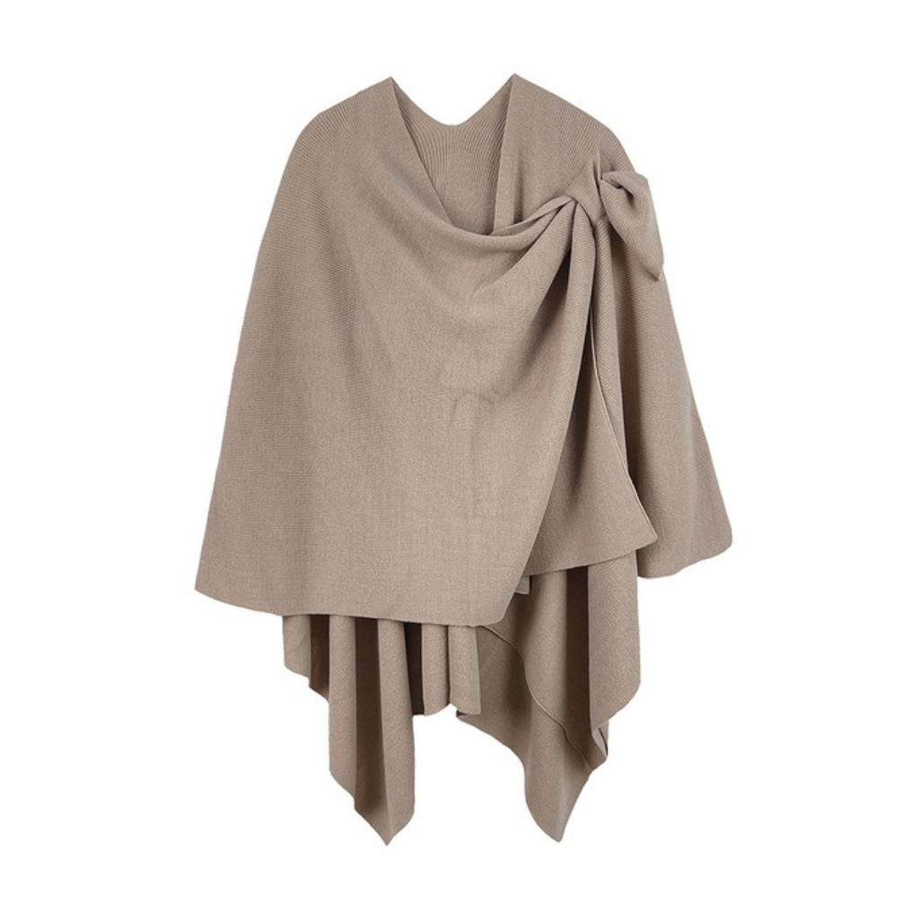 The Soft Solid Color Ruana with Strap Hold by FASHION GO is a beige knitted shawl featuring an asymmetrical draped design and a bow on one side.