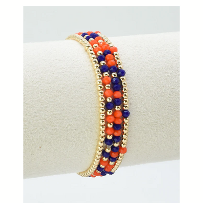 FASHION GO Set of 4 Glass Bead and Gold Stretch Bracelets—perfect for gameday—features gold, orange, and dark blue beads to show off your team colors, displayed on a white cylindrical stand.