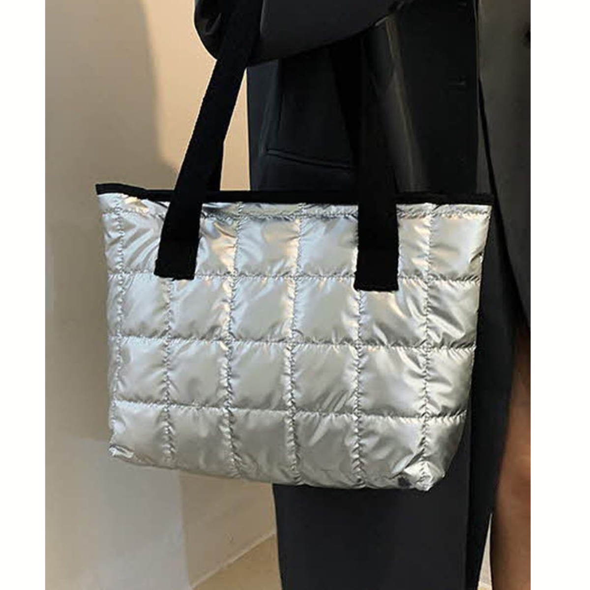 A person holding the FASHION GO Quilted Shoulder Tote Bag - Assorted Colors, styled with black handles and a dark coat.