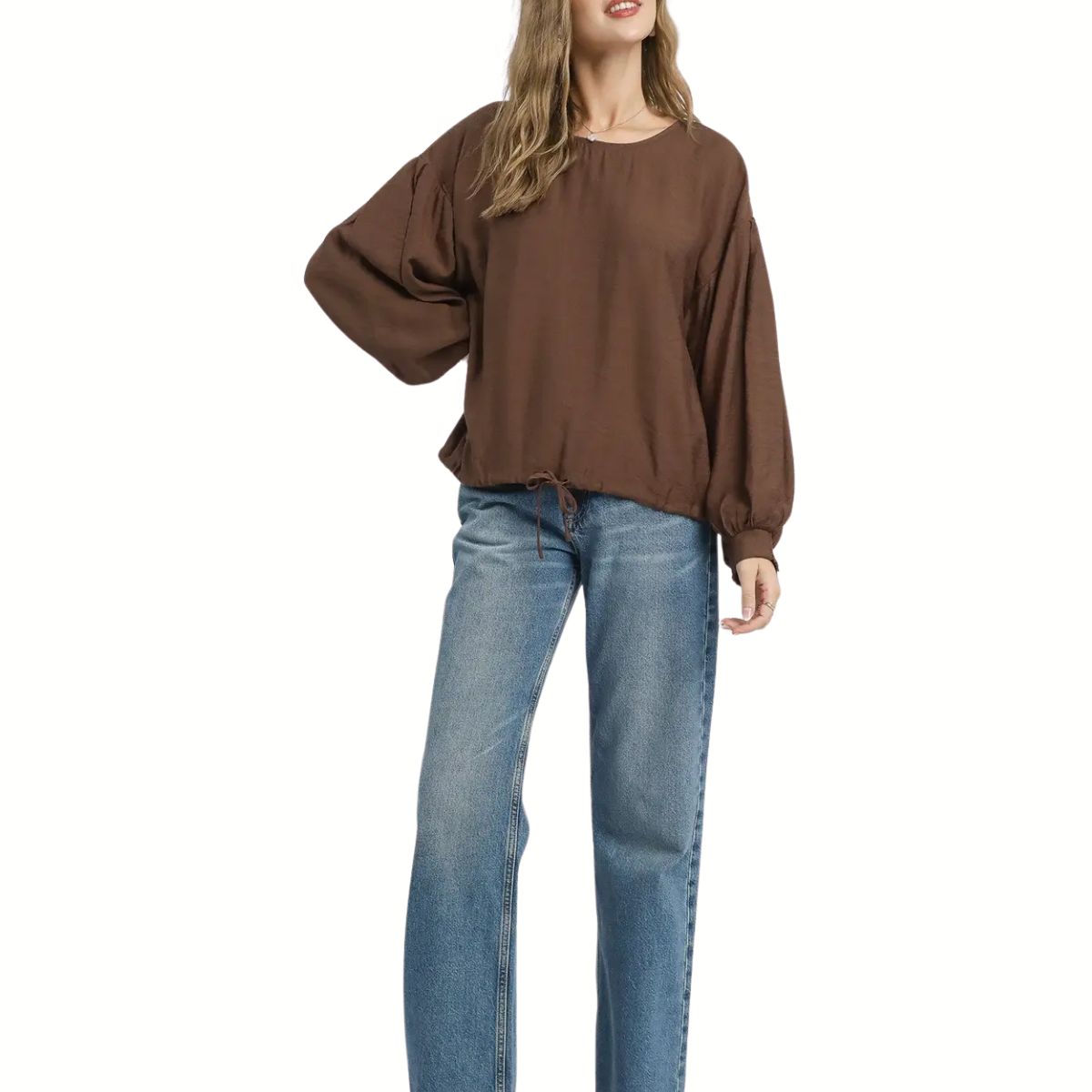 A person in an Umgee Round Neck Long Sleeve Drawstring Blouse and blue wide-leg jeans stands against a white background.