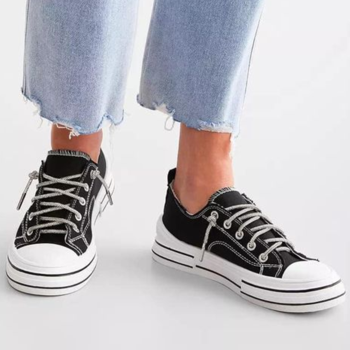Close-up of a person wearing light blue frayed-hem jeans and VERY G's Aman Tennis Shoe in black with a canvas upper. Main image
