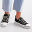 Close-up of a person wearing light blue frayed-hem jeans and VERY G's Aman Tennis Shoe in black with a canvas upper.