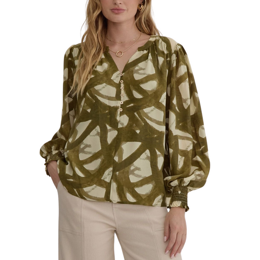 Woman wearing the Slash Print Lightweight Blouse in Olive by Entro, beige pants, and gold jewelry, including a necklace and earrings. She is standing with one hand in her pocket.