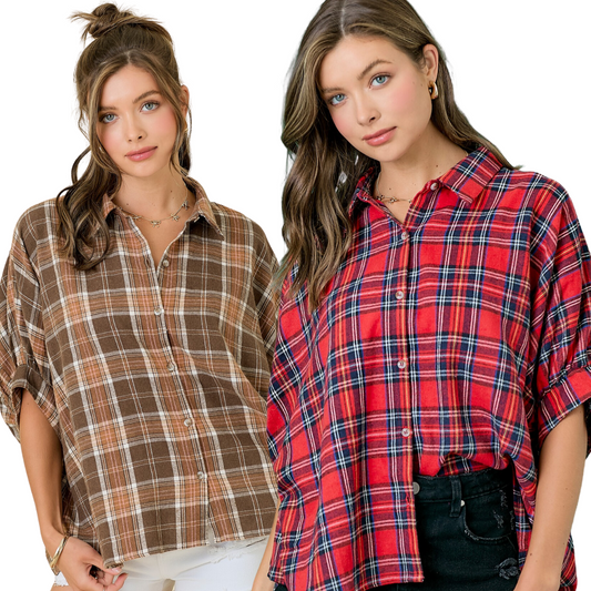 Two women are dressed in casual plaid shirts from FASHION GO; one is wearing a Plaid Oversized Button Down Shirt in a brown plaid pattern with short sleeves, while the other sports a red Updated Flannel. Both have long hair and neutral expressions.