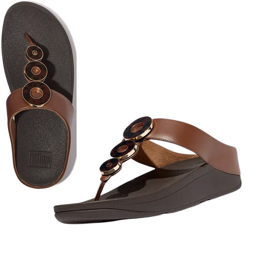 A pair of Fino Resin Hoop Flip Flops by FIT FLOPS in brown, featuring circular decorative elements, black cushioned soles, and Microwobbleboard™ midsoles for extra comfort.