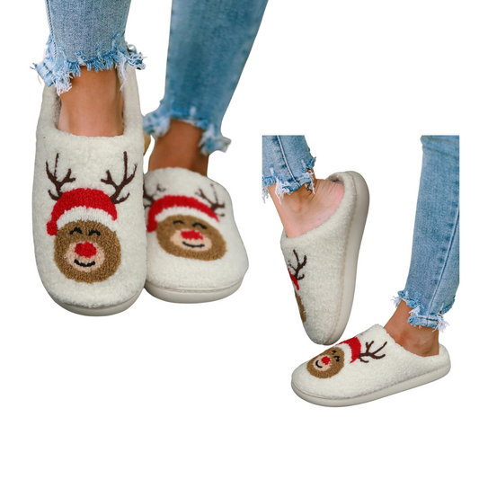 Close-up of feet wearing Shewin's Christmas Deer Pattern Home Plush Slippers featuring a reindeer face with a Santa hat design. The person is also wearing blue ripped jeans and is standing on one foot.