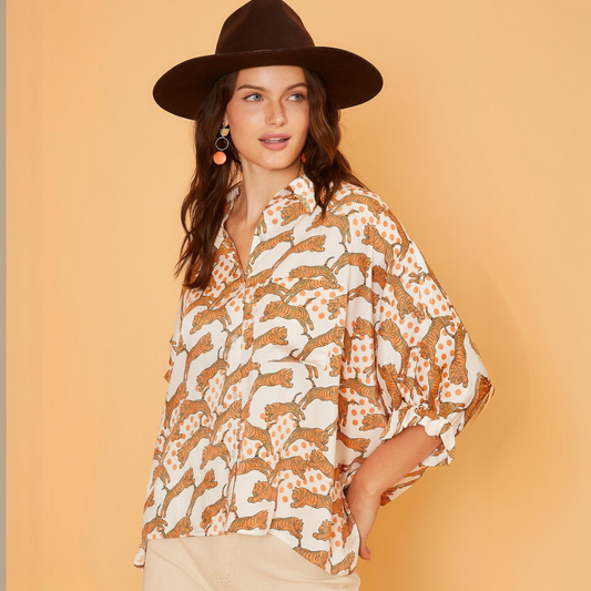 A person wearing a wide-brimmed hat and the Zenana Tiger Printed Oversized Blouse poses against an orange background.