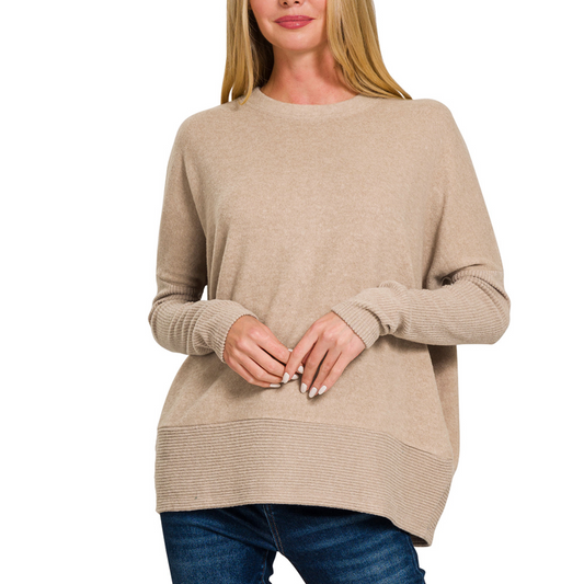 A person in an Ash Mocha Brushed Hacci Dolman Sleeve Sweater by Zenana and blue jeans is standing with their hands clasped.