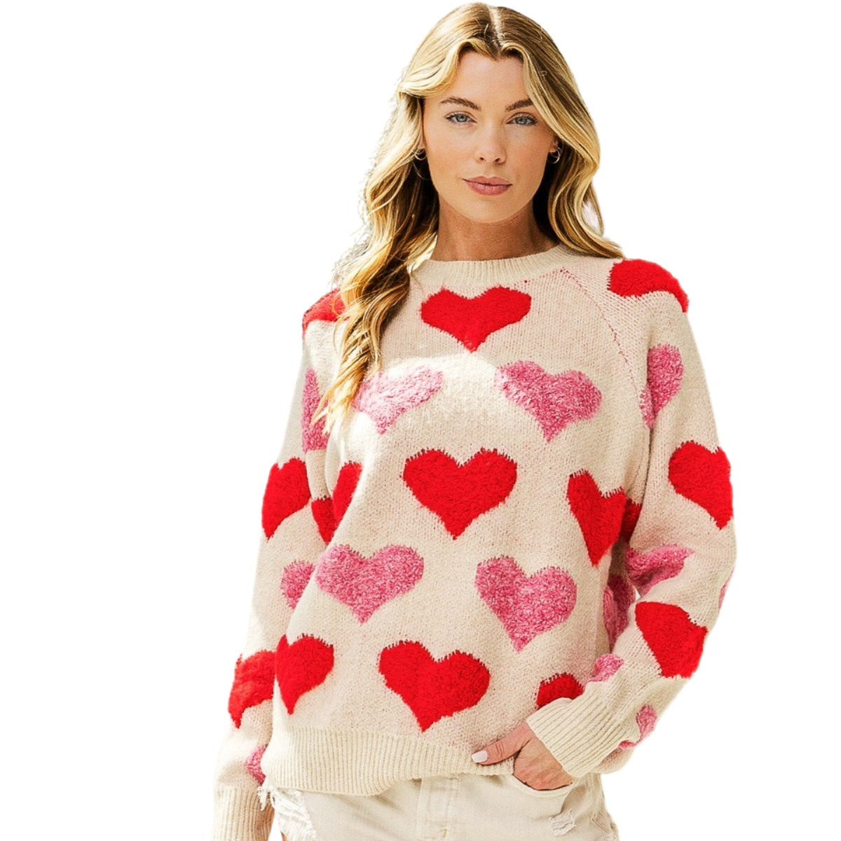 A woman models the FASHION GO Heart Raglan Sleeve Sweater featuring red and pink heart patterns, standing with one hand in her pocket against a white background.