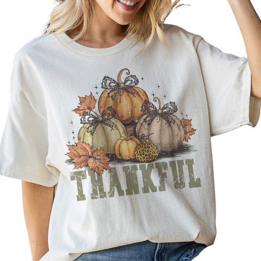 A woman wears the FASHION GO THANKFUL PUMPKINS Oversized Graphic Tee, a white unisex shirt with an illustration of pumpkins, leaves, and "THANKFUL" printed beneath the design.