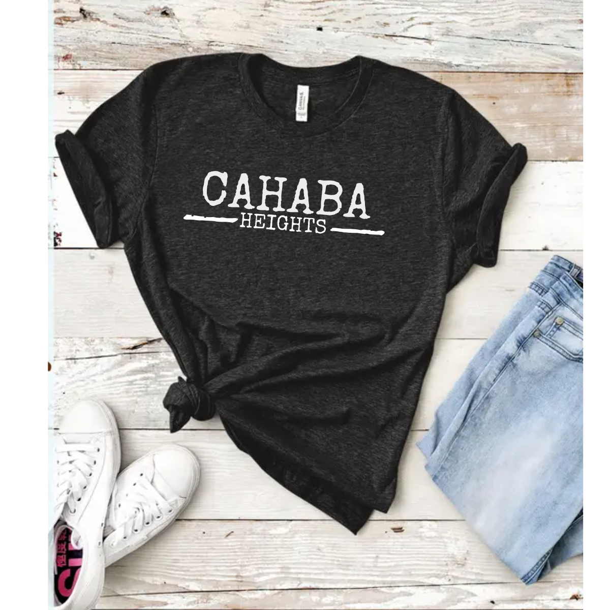 A streetwear-inspired Faire Distressed Front Cahaba Heights T-Shirt in dark grey with "CAHABA HEIGHTS" in white, paired with light blue denim shorts and white sneakers on a wooden backdrop. Main image