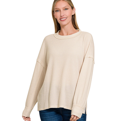A woman smiles while wearing the Zenana Brushed Ribbed Hacci Drop Shoulder Sweater and blue jeans, standing against a plain white background.