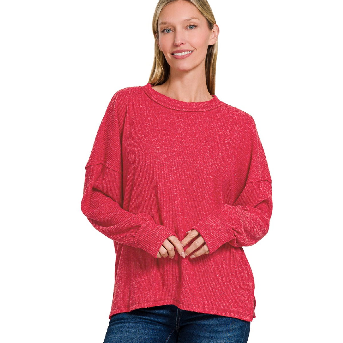 A woman stands smiling in a Zenana Brushed Ribbed Hacci Drop Shoulder Sweater and blue jeans against a plain white background.