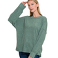 A woman wearing a loose-fitting Zenana Brushed Ribbed Hacci Drop Shoulder Sweater in green and blue jeans stands against a white background.