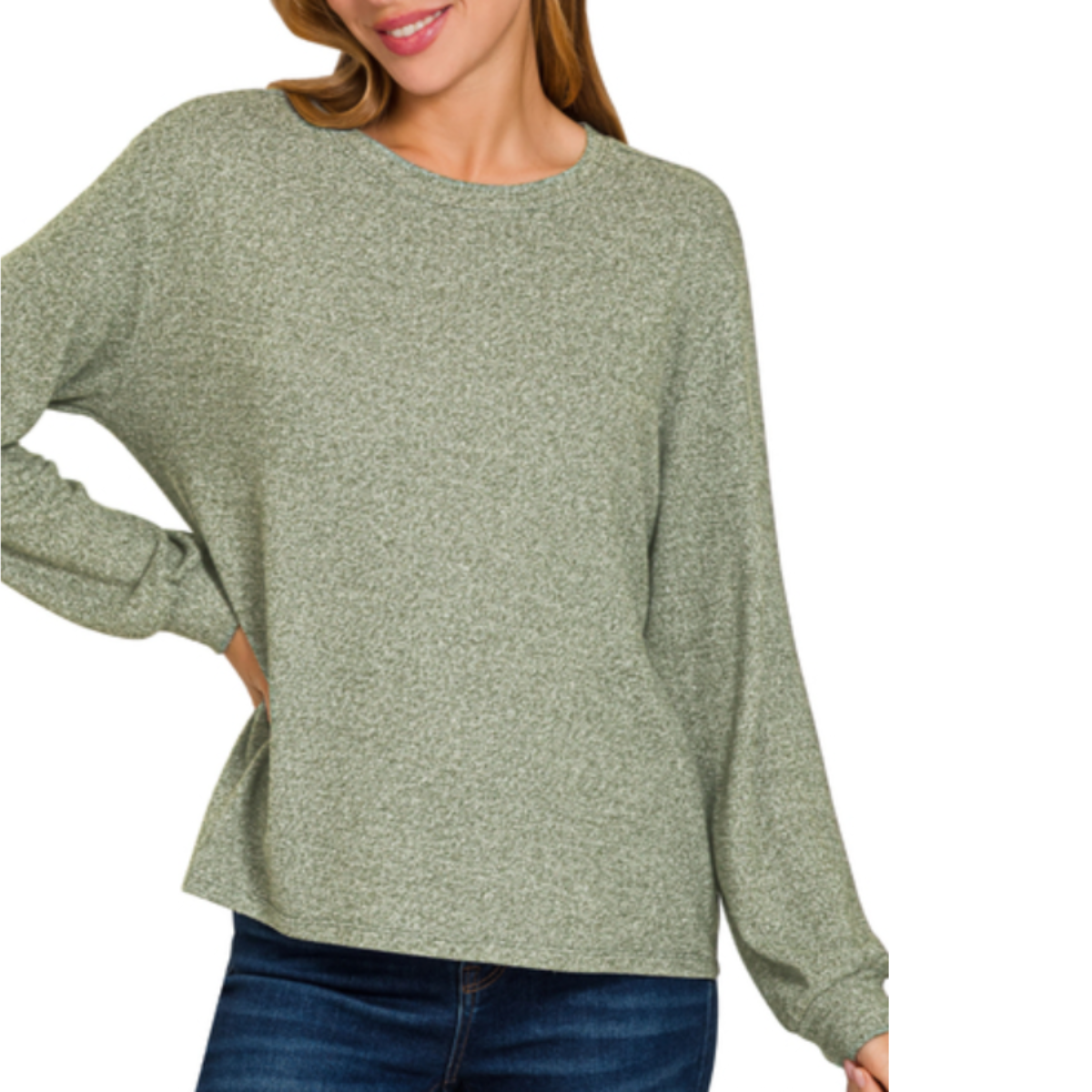 A woman models the Zenana Soft Melange Hacci Round Neck Long Sleeve Tee in light green with blue jeans, standing with one hand on her hip against a white background.