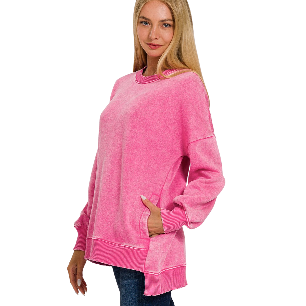A woman wears the FASHION GO Acid Washed Fleece Hi-Low Pullover, a loose-fitting, long-sleeve pink sweatshirt with ribbed cuffs and hem, paired with blue jeans, standing against a white background.