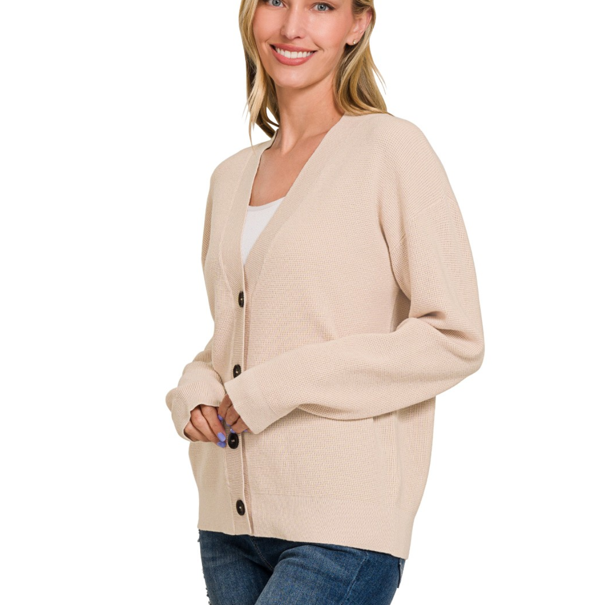 A woman stands smiling in a Zenana Cardigan Sweater—beige, button-front—layered over a white top with blue jeans.