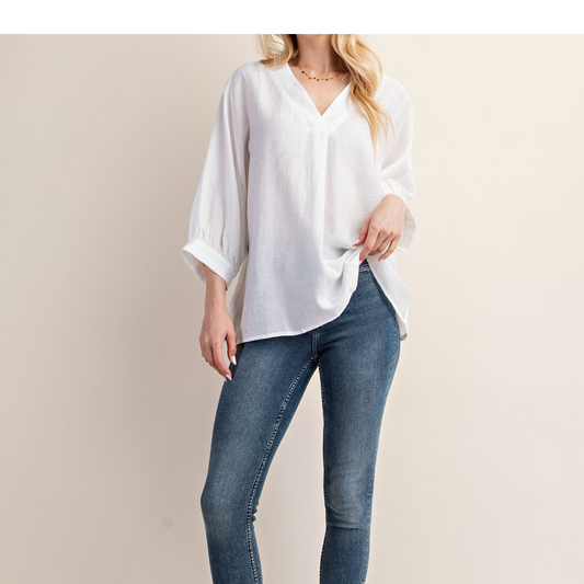 A person wearing the V-Neck Loose Fit Blouse in White by GiGiO from FASHION GO and blue jeans stands against a plain background.