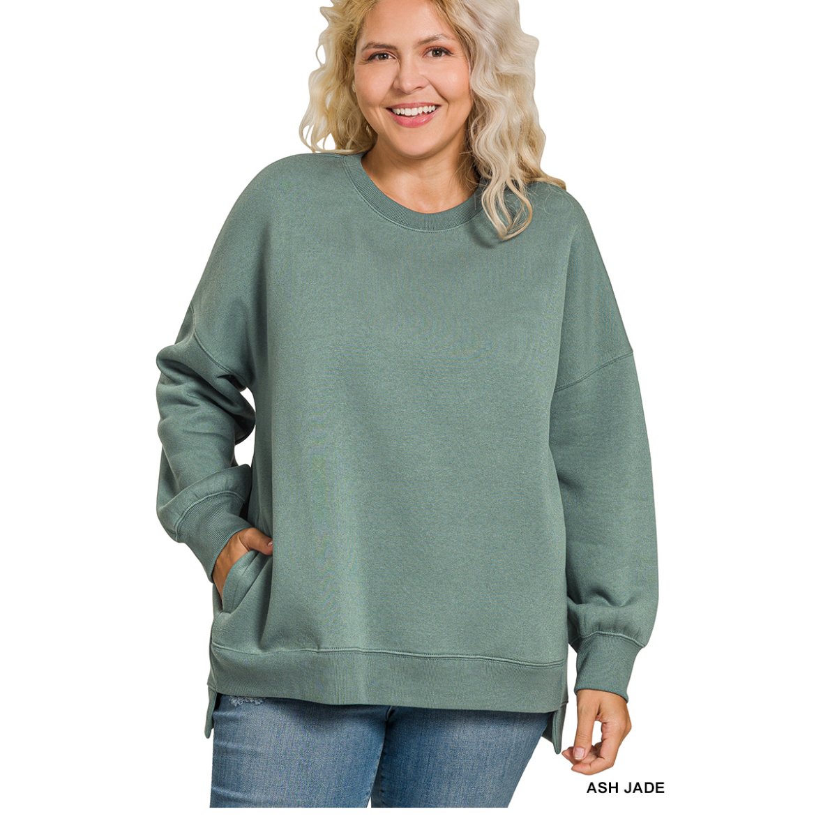 A woman models the Zenana Plus Fleece Hi-Low Sweatshirt with Pockets in ash jade green, styled with blue jeans against a white background. Main image