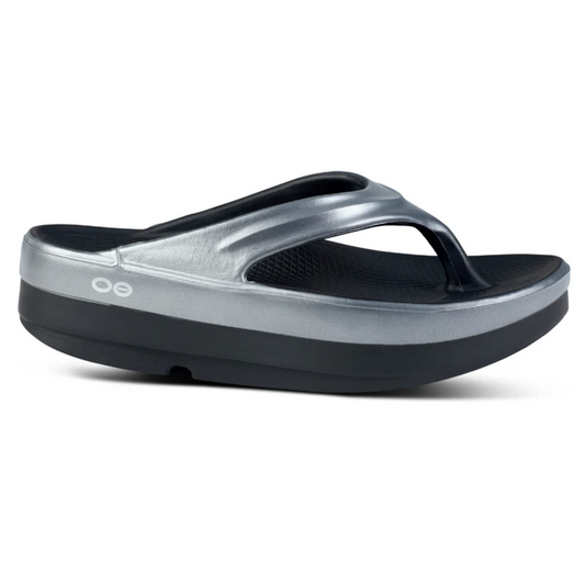 Side view of the Oomega Oolala Luxe Women in Basalt by Oofos sandal, showcasing a silver and black design with a thick, cushioned sole featuring OOfoam technology and branded with the OOFOS LLC logo on the side, perfect for active recovery.