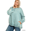 A woman models the FASHION GO Plus Acid Washed Fleece Hi-Low Hem Pullover in ash blue with blue jeans, posing against a white background with one hand on her neck and the other in her pocket.