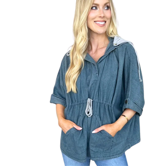 A woman models the Carole Christian Denim Shirt Jacket with Detachable Hood, featuring a loose fit, soft blue denim, drawstring waist, and pockets, standing against a white background.