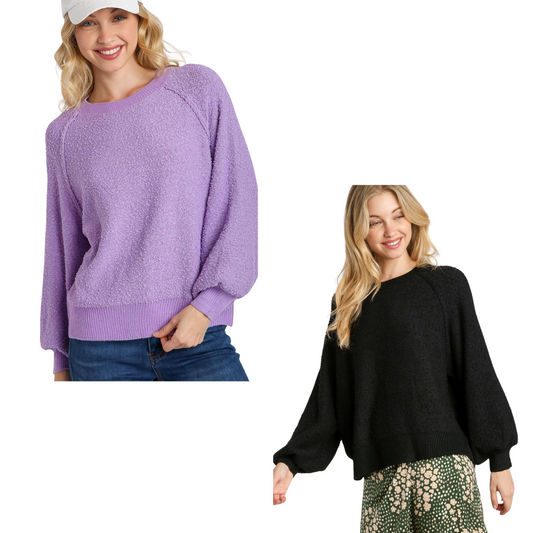 Two women stand against a white background: one wears the Umgee Puff Sleeve Boat Neck Sweater in light purple with jeans and a cap, while the other pairs a black polyester-acrylic sweater with a floral skirt.