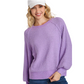 A woman smiles in a Umgee Puff Sleeve Boat Neck Sweater in textured lavender, paired with blue jeans and a white cap, standing against a white background.