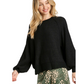 A woman wears the Umgee Puff Sleeve Boat Neck Sweater in black, styled with a green skirt featuring a white floral pattern, against a white background.