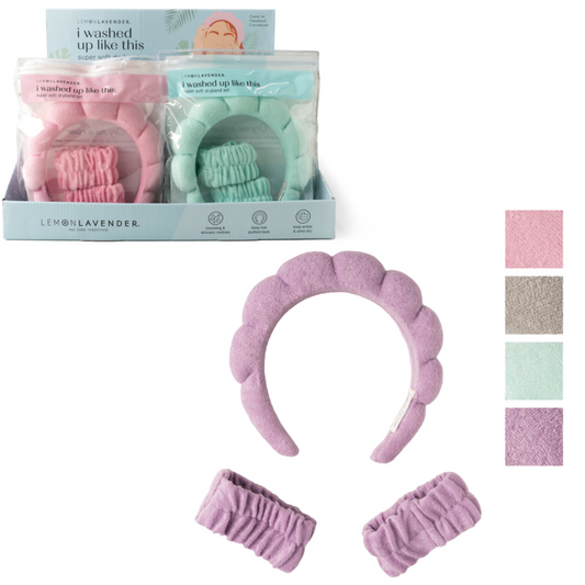 Displayed are a pink terrycloth headband and two matching scrunchies, ideal for skincare routines. They come in a "DM MERCHANDISING INC" box with blue and pink variants shown in the background and are part of the "I Washed Up Like This Dryband Headband Set.