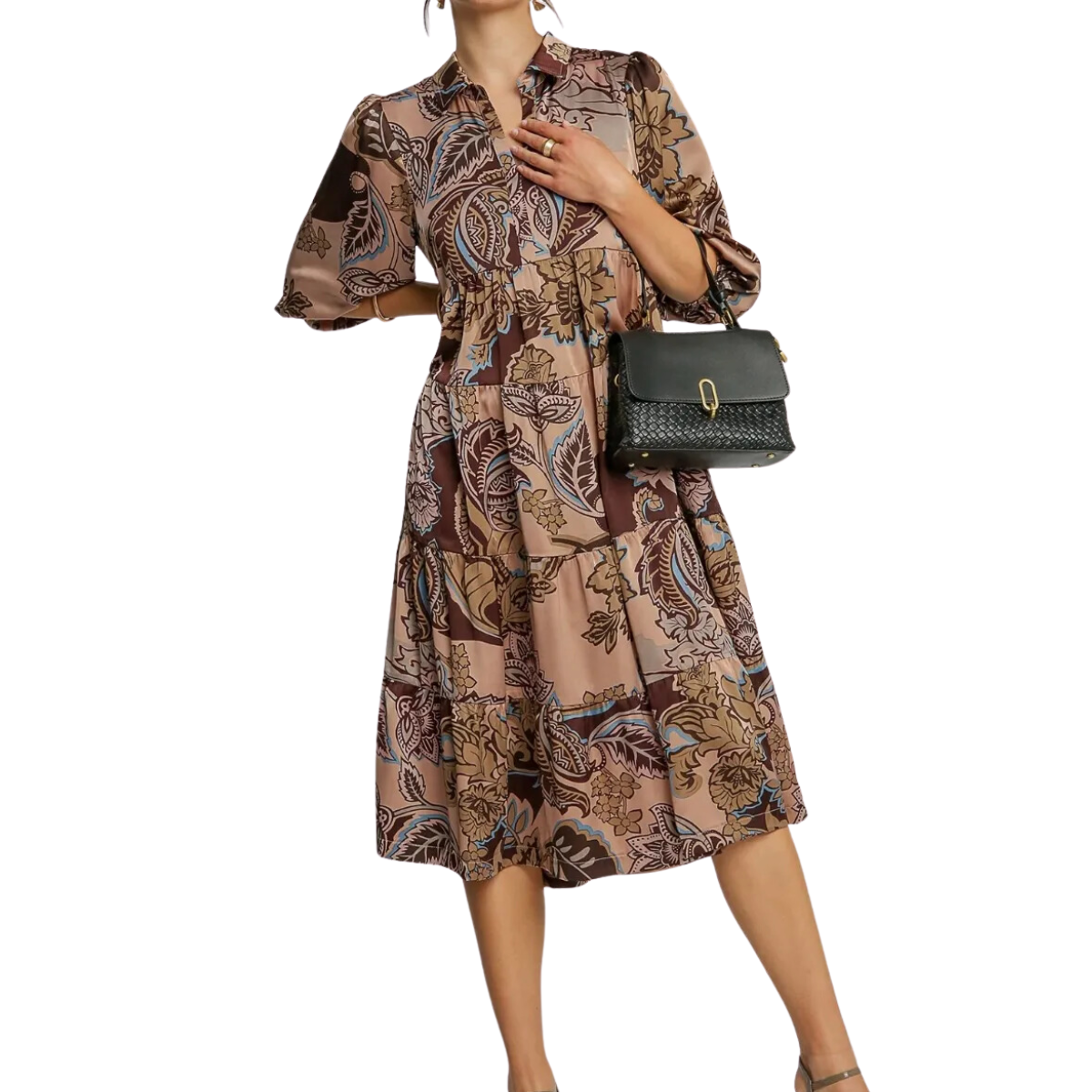 A woman in a brown Paisley Print Satin Midi Dress by Umgee, characterized by a collared split neck and tiered puff sleeves, holds a black handbag.