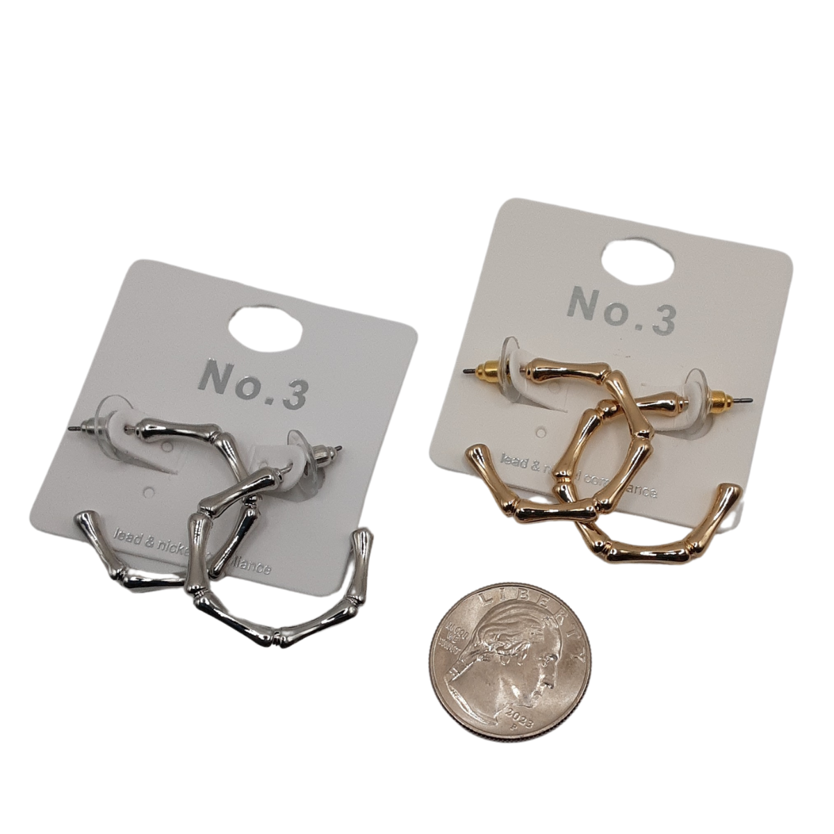 Two pairs of the Bamboo Look Hoop Earrings from SPECIAL EFFECTS, one in silver and one in gold, each with a 1-inch diameter, are elegantly presented on display cards labeled "No. 3." A quarter is placed below for size reference.