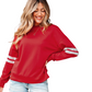 A smiling woman with long hair wears the FASHION GO Varsity Striped Drop Shoulder Sweatshirt in red and light denim shorts, standing against a white background.