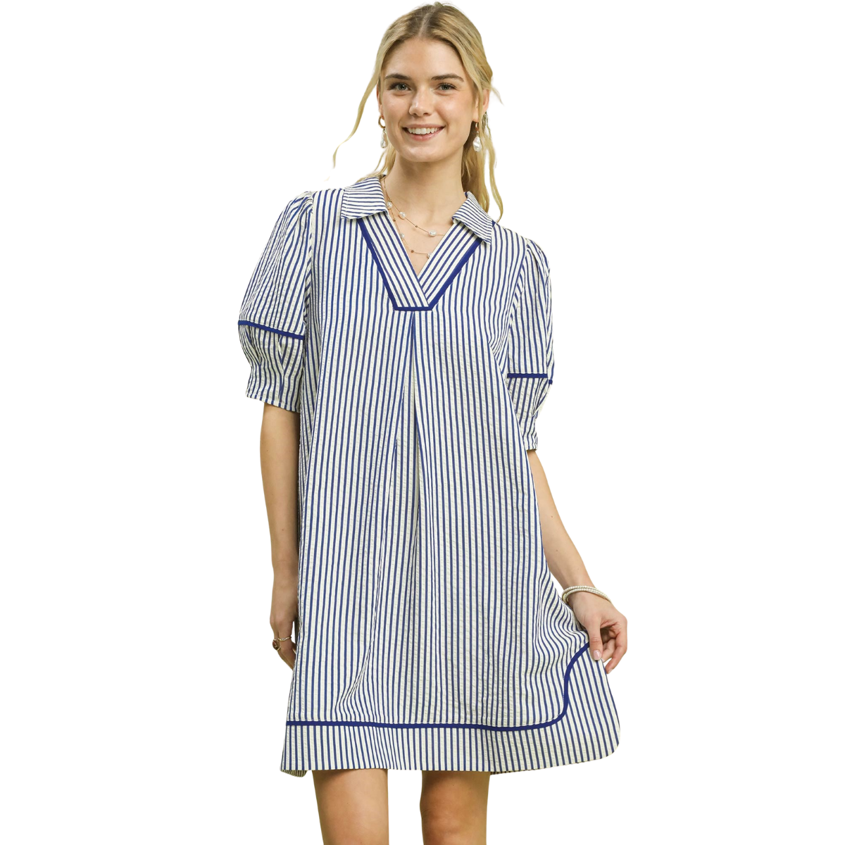 A woman wearing the Umgee Stripe Collared Shift Dress—a loose-fitting, short-sleeve dress with blue and white stripes—stands and smiles at the camera. Main image