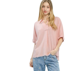 A woman wears the Umgee Linen Frayed Edge Split Neck Short Sleeve Top in light pink, styled with blue embroidered jeans. She stands with one hand in her pocket against a white background.