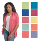 A woman wears the ganz Button Wrap in pink over a white top and jeans. Beside her, ten fabric swatches in different colors display this travel essential’s multiple styling options.