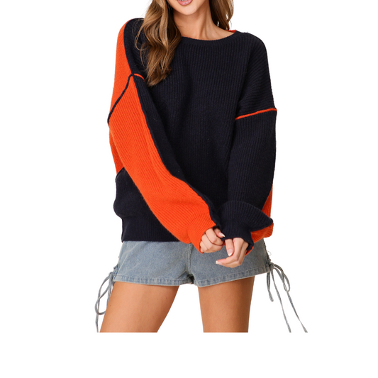 A person is wearing the Gameday Oversized Sweater by Lumiere in Navy/Orange from FASHION GO, paired with denim shorts featuring lace-up details.