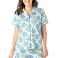 A woman is smiling in the Hello Mello Lounge Top Spring Edition by DM MERCHANDISING INC, a short-sleeve button-up pajama set with blue patterns and vibrant yellow lemon prints, offering an ultra-soft feel and relaxed fit.