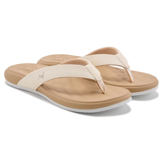 The Cushion Melody Flip Flops in Sand by REEF are beige flip-flops with white straps and tan footbeds, featuring a cushy textured surface for comfort and support, enhanced with memory foam.