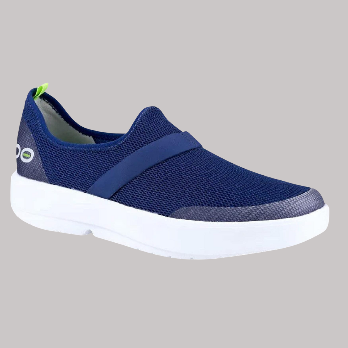 The OOFOS OMG LOW MESH NAVY Mens by OOFOS LLC is a blue slip-on sneaker with breathable material and a white sole, accented with a green pull tab at the heel, set against a plain gray background.