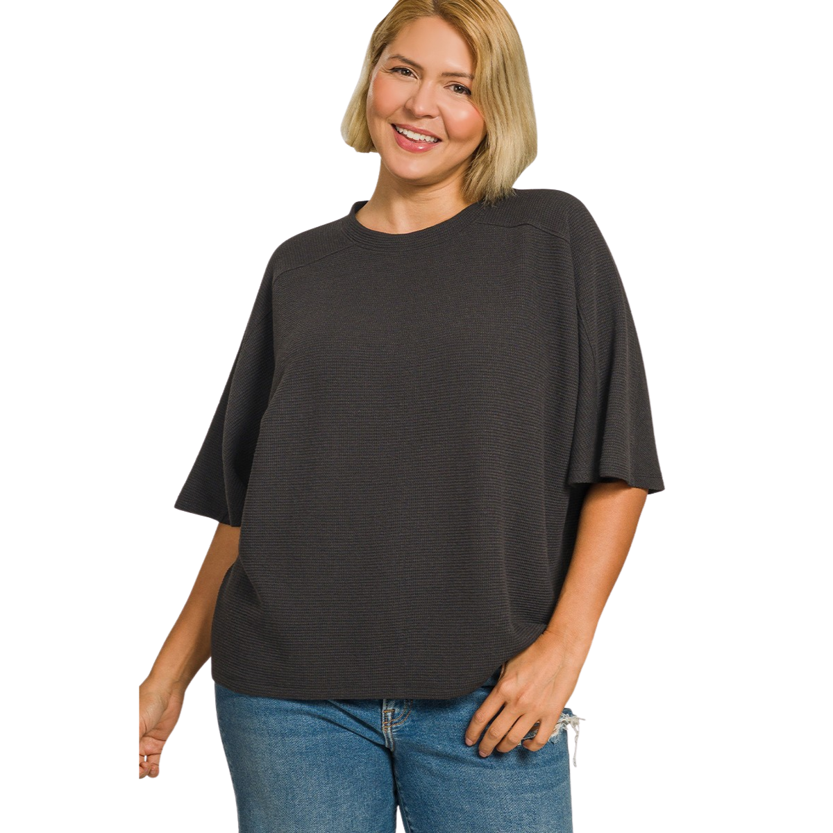 A smiling person with short blonde hair wears the Zenana Double Knit Short Sleeve Top Plus Sizes in dark gray and blue jeans, standing against a white background.